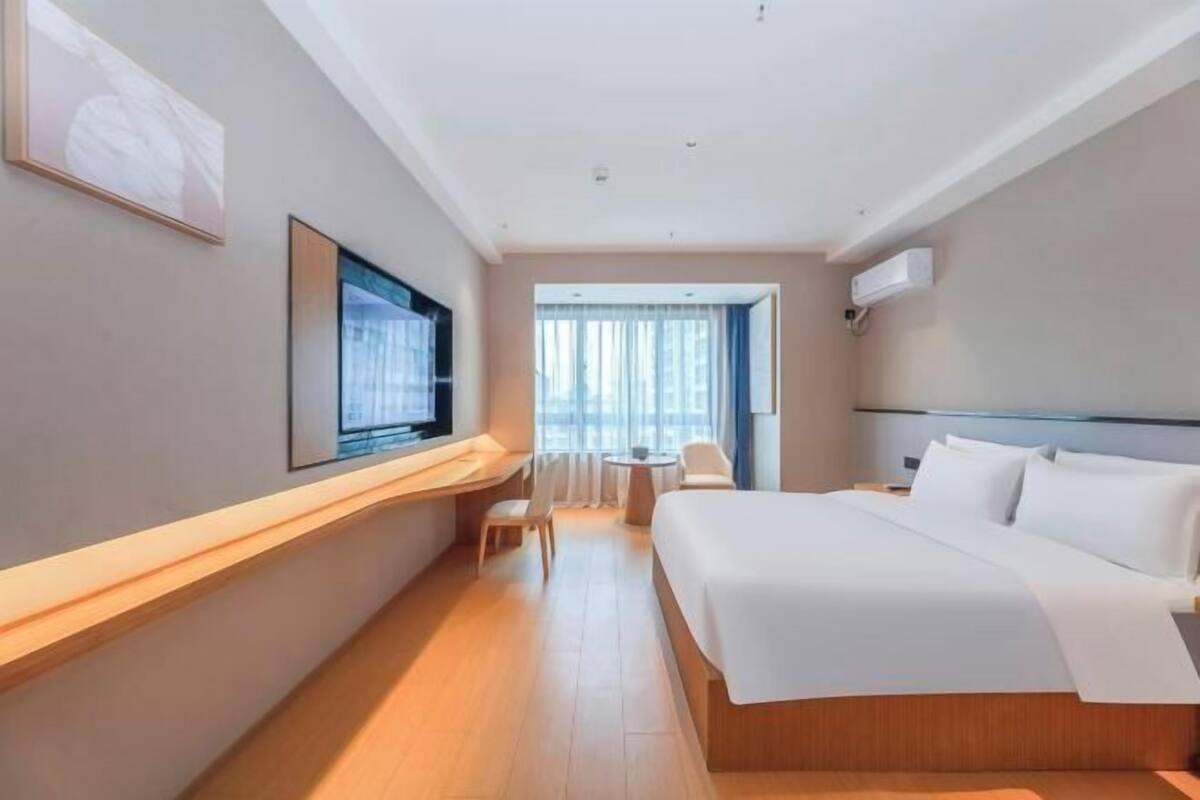 Een hotelkamer met een groot bed, een bureau, een stoel, een televisie en een raam met gordijnen.
