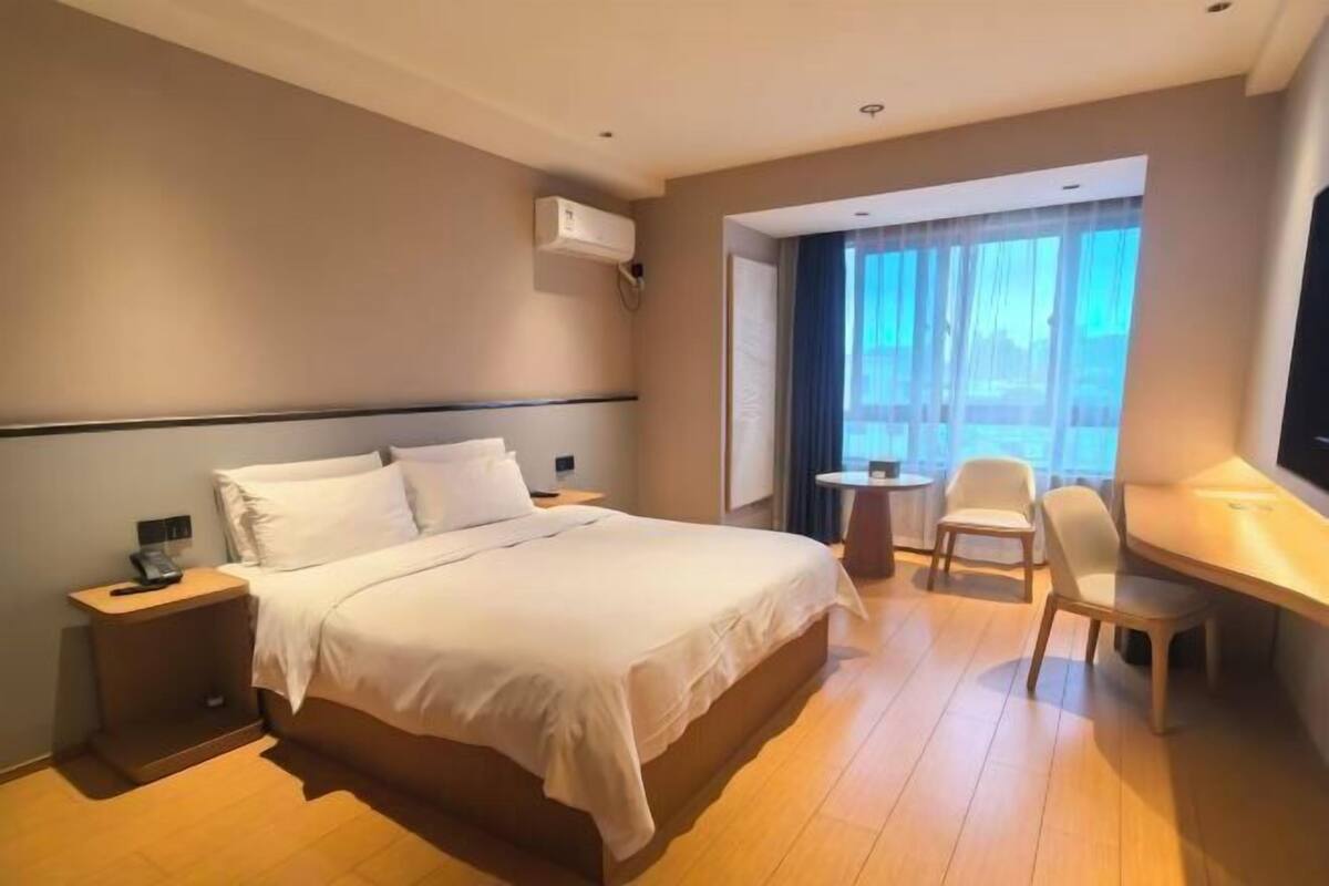Een hotelkamer met een bed, nachtkastje, stoel, bureau en een raam met gordijnen.