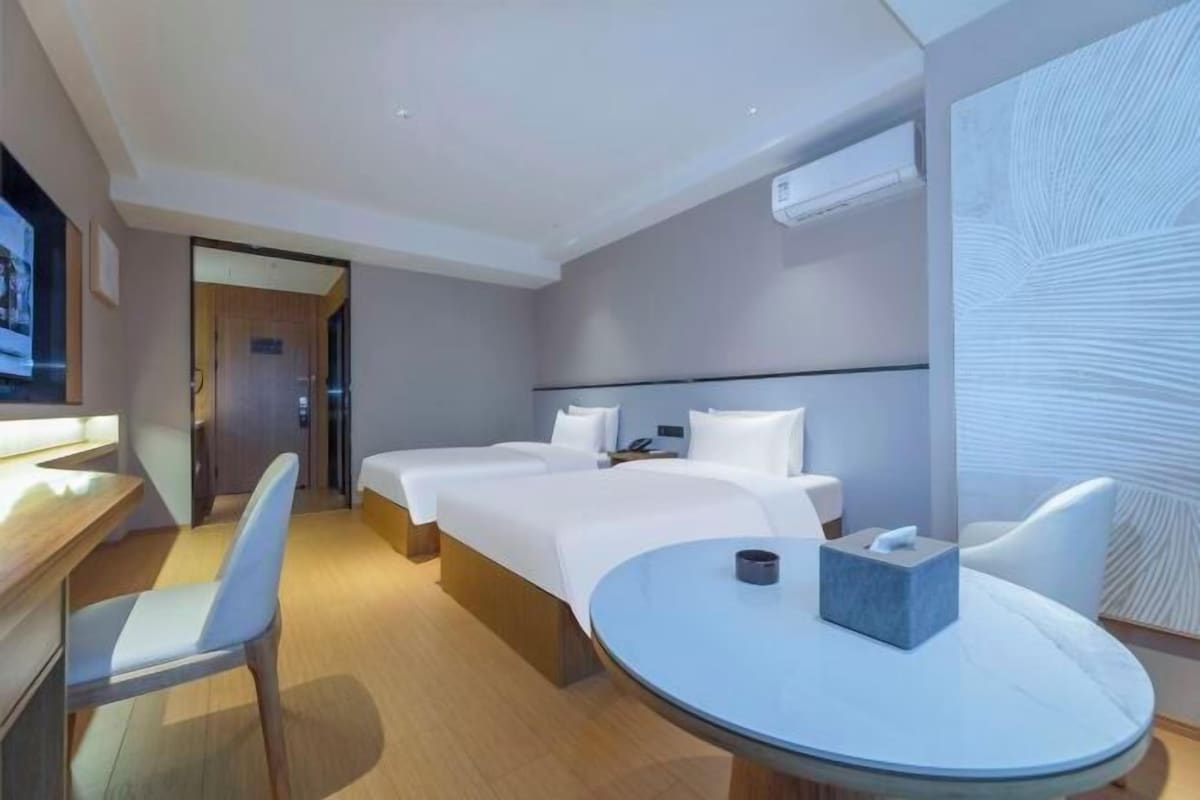 A modern hotel room with two beds, a desk, and a round table.