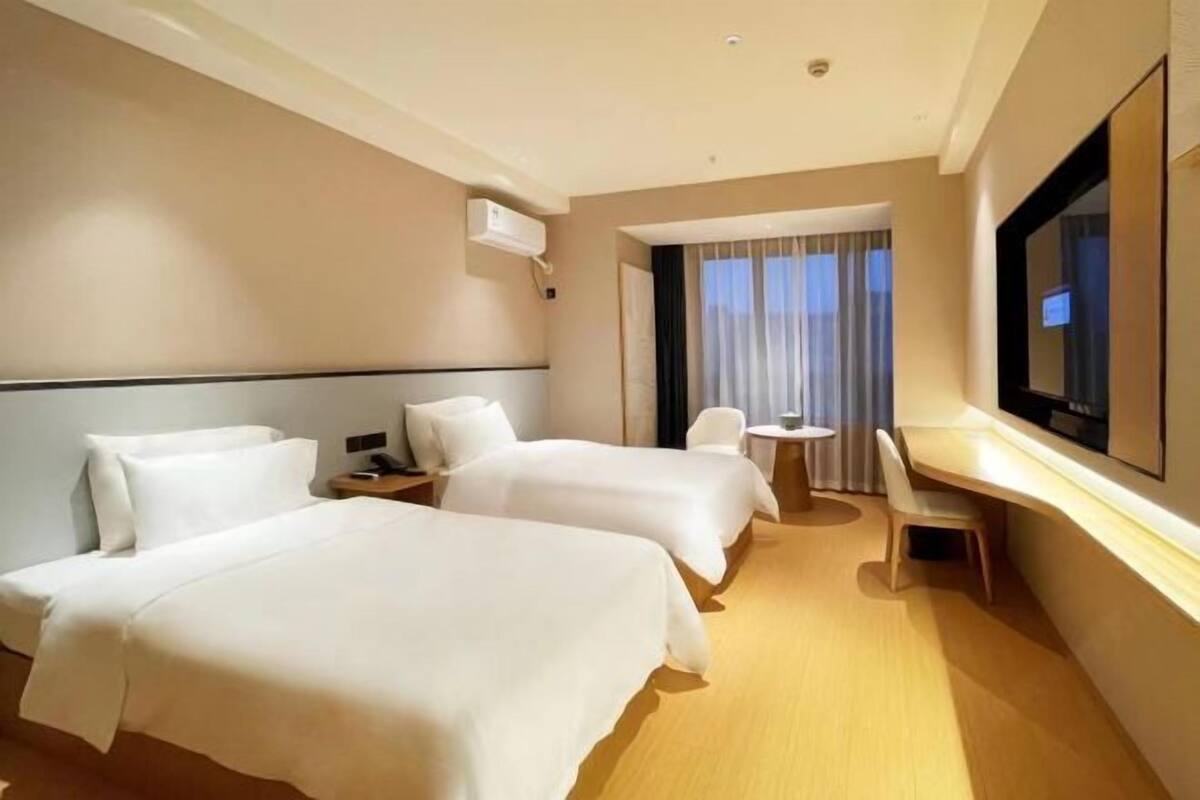 Een hotelkamer met twee bedden, een bureau, een stoel, een televisie en een raam met gordijnen.