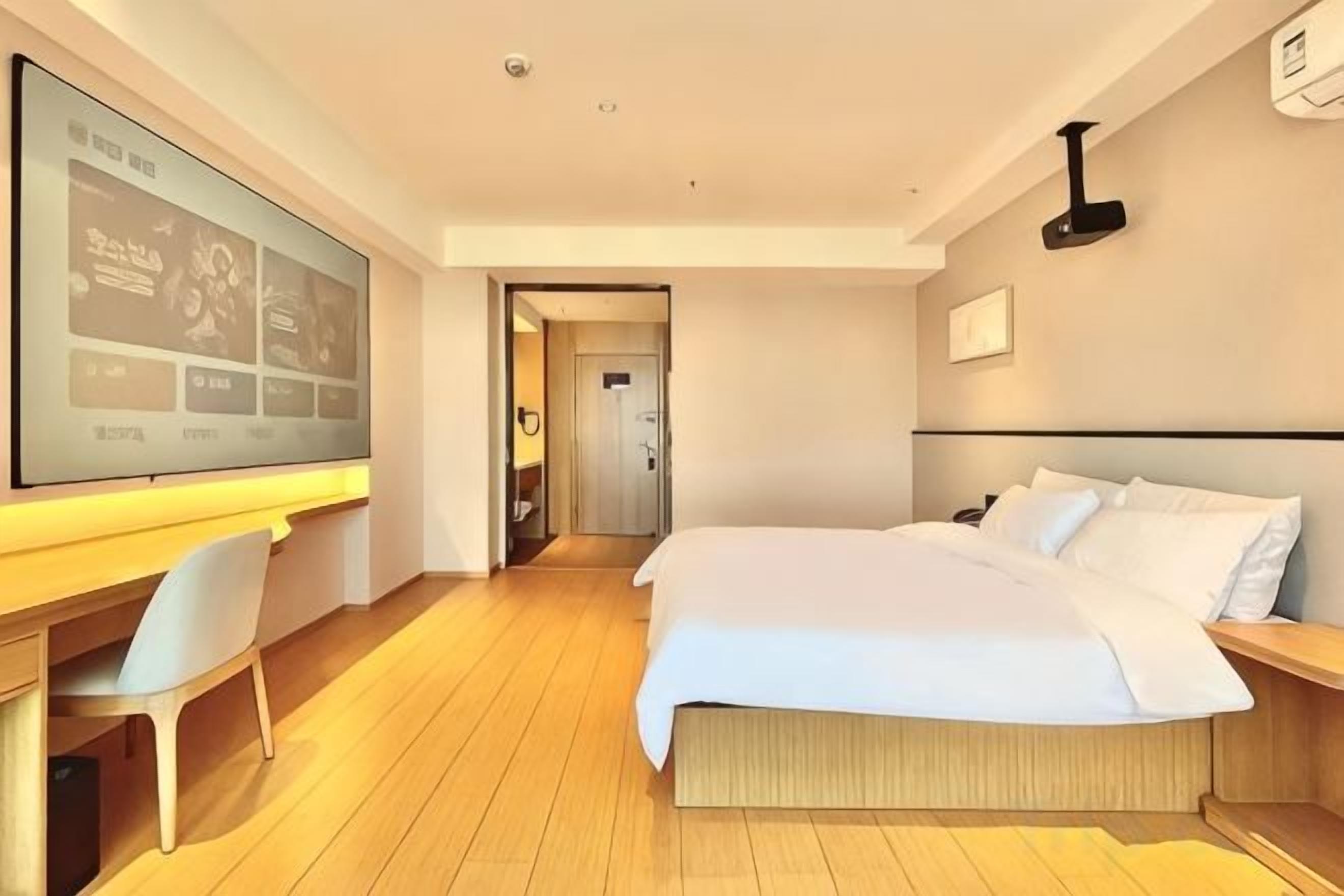 A hotel room with a bed, desk, chair, and a large screen.
