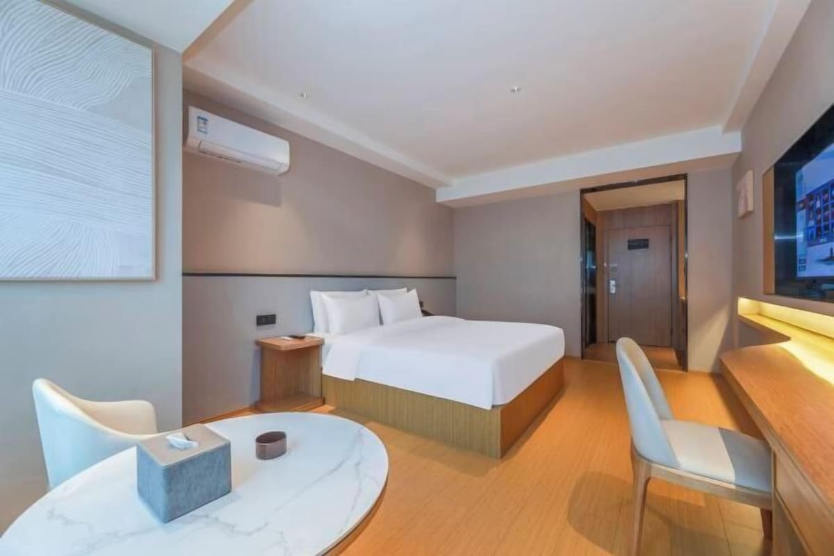 A hotel room with a bed, a desk, a chair, a table, and a TV.