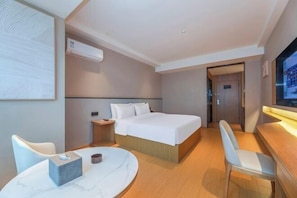 A hotel room with a bed, a desk, a chair, a table, and a TV.