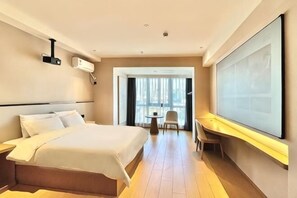 Hotellihuone, jossa on sänky, työpöytä, tuoli ja suuri ikkuna.