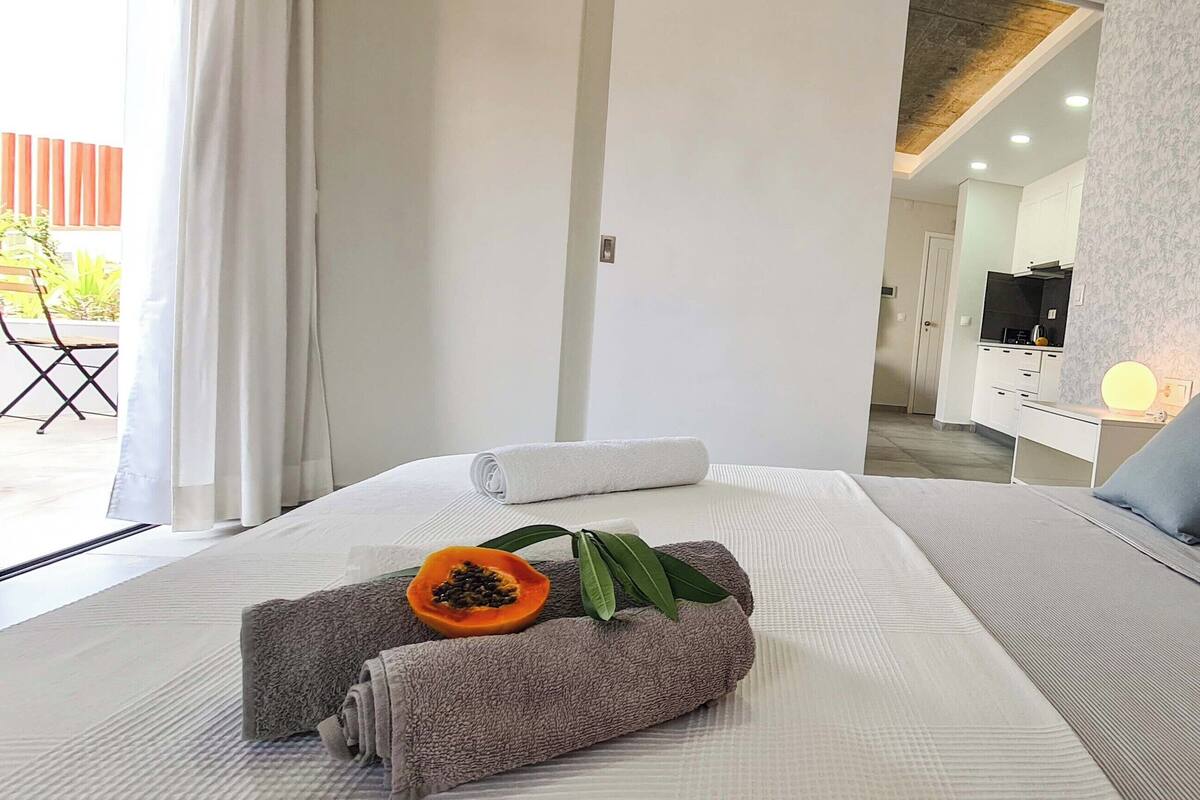 A hotel room with a bed, pillows, a nightstand, a TV, and a bathroom visible in the background.
