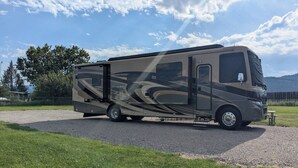 A recreational vehicle parked on a gravel path with a grassy area and trees in the background.