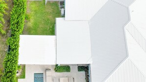 Et luftfoto af et hus med swimmingpool, omgivet af et hvidt hegn og frodig vegetation.