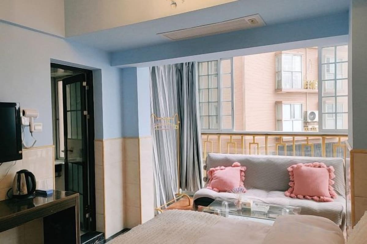 A bedroom with a bed, a TV, a window with curtains, and a view of a building outside.