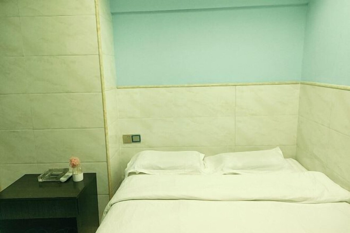 A hotel room with a bed, a nightstand, and a small table with a vase and a book.