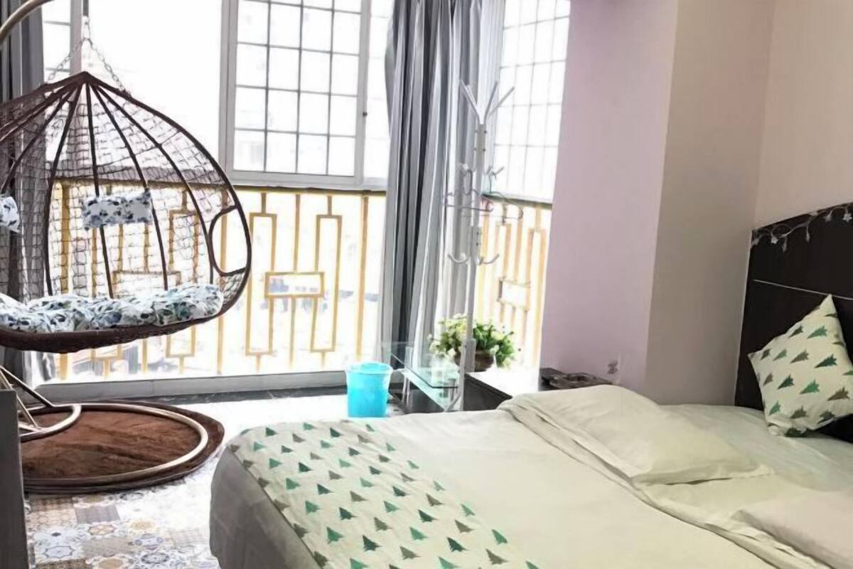 Ein Schlafzimmer mit Bett, Hängesessel, einem Fenster mit Vorhängen und einem Balkon mit Geländer.