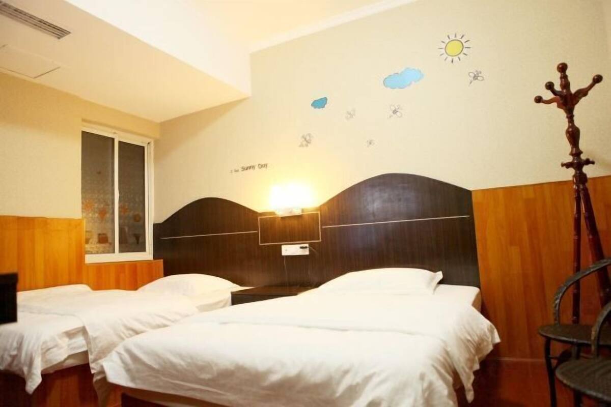 Ein Hotelzimmer mit zwei Betten, Holz-Kopfteilen, einer Wandlampe und einem Fenster mit Jalousien.