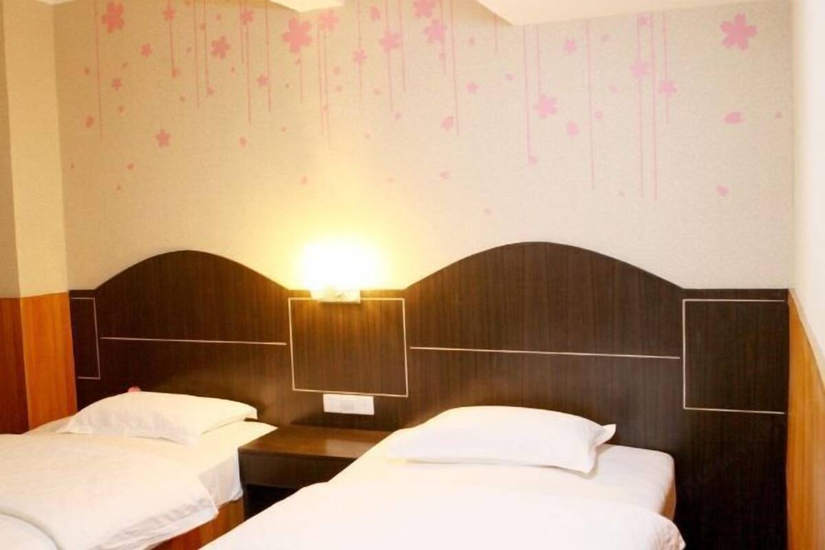 Ein Hotelzimmer mit zwei Einzelbetten, Holz-Kopfteilen und einer Wand mit Blumenmuster.