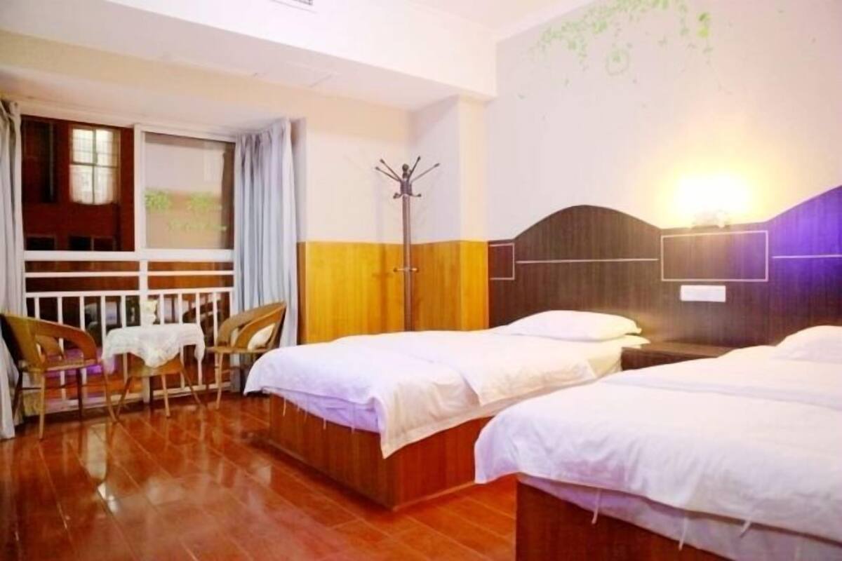 Ein Hotelzimmer mit zwei Betten, Holzboden, Kleiderständer und einem Tisch mit Stühlen.