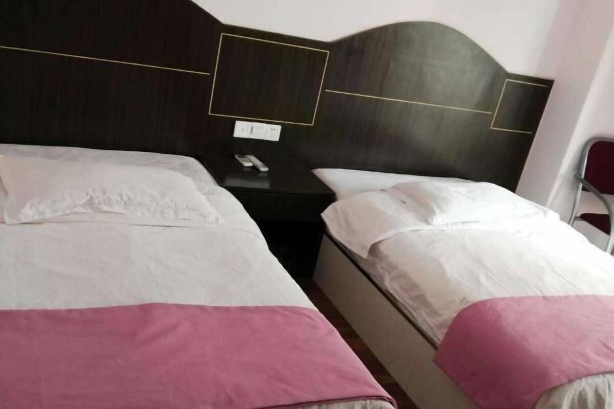Ein Hotelzimmer mit zwei Betten, jeweils mit weißer Bettwäsche und einer rosafarbenen Decke. Ein Nachttisch mit Telefon und ein kleiner Tisch befinden sich zwischen den Betten.