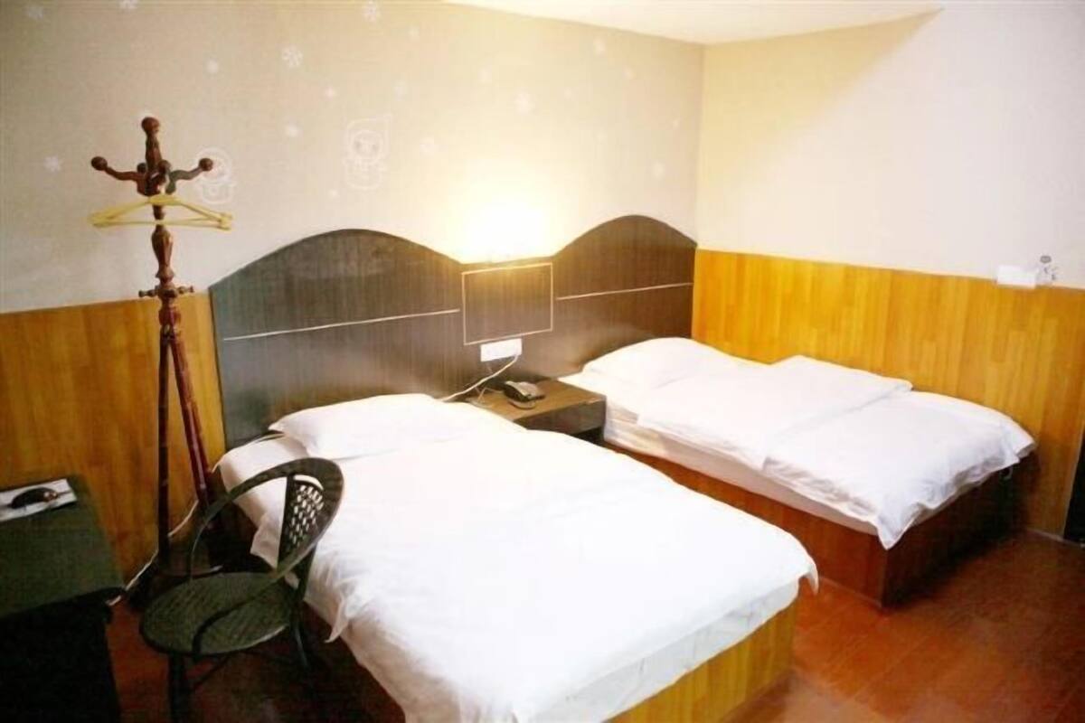 Ein Hotelzimmer mit zwei Einzelbetten, einem Holz-Kopfteil, einem Schreibtisch mit Stuhl und einem Wandhaken für Kleidung.