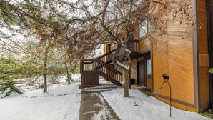 Ein Holzgebäude mit einer Treppe, die zu einem Balkon führt, umgeben von verschneitem Gelände und Bäumen.