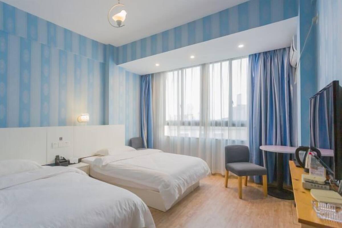 A hotel room with two beds, a desk, a chair, a TV, and a window with curtains.