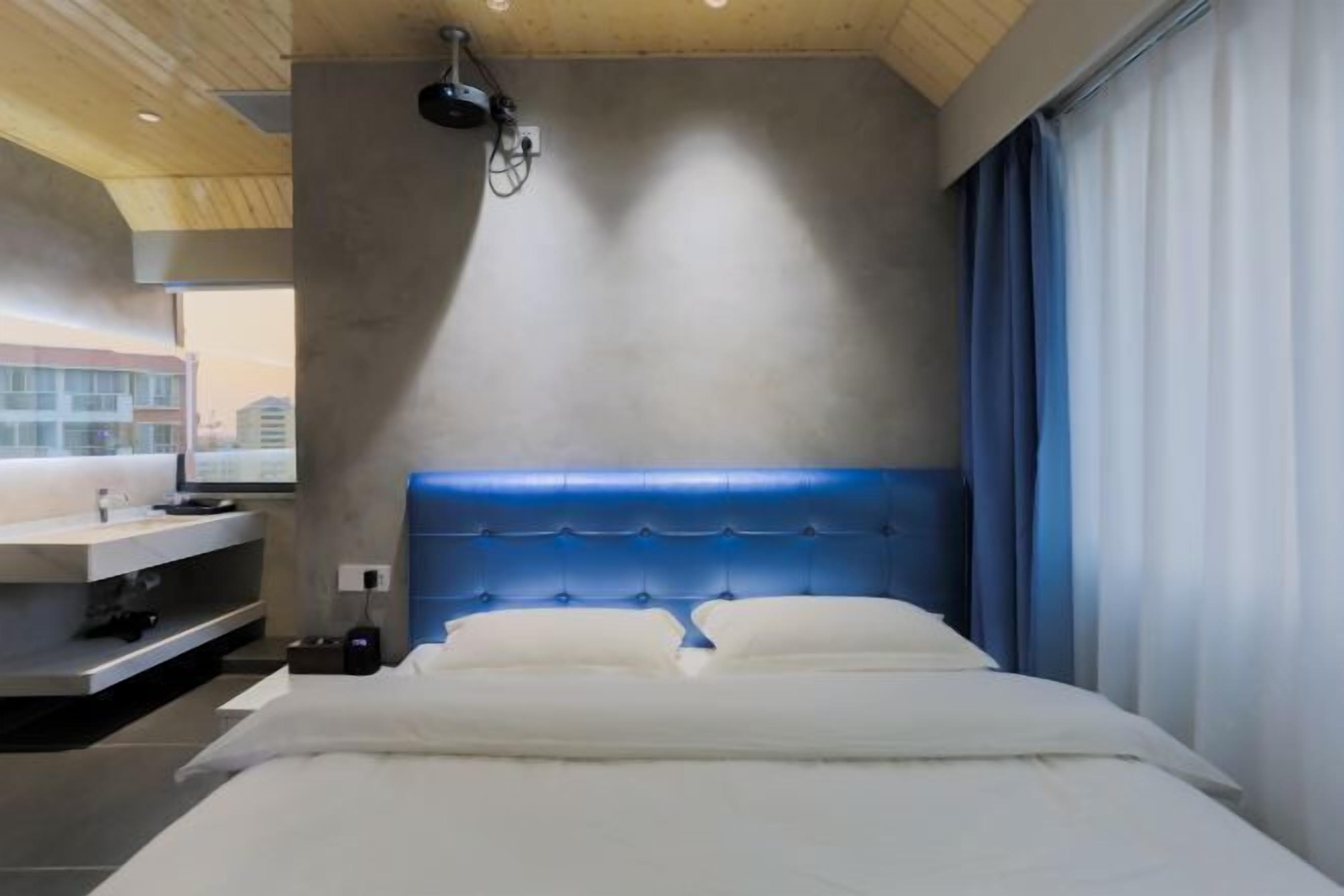 A modern hotel room with a large bed, a headboard, a bedside table, and a window with curtains.