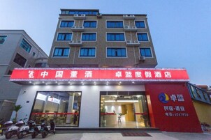 A hotel with a red signboard, a glass entrance, and a parking area with scooters.