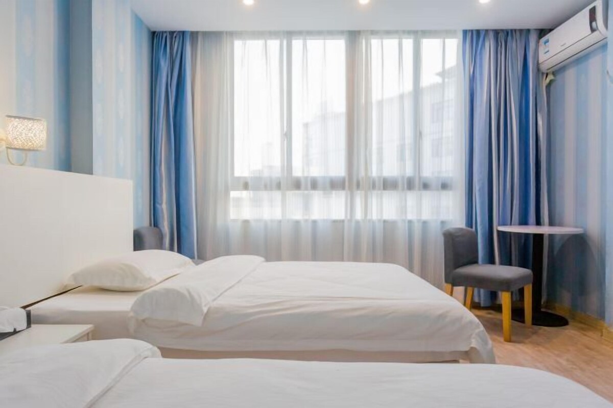 Habitación de hotel con dos camas, una mesita, una silla y una ventana con cortinas.