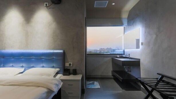 A modern bedroom with a bed, bedside table, and a view of the cityscape through a window. - Dongshan Zhuolan Resort Hotel (Dongshan County)