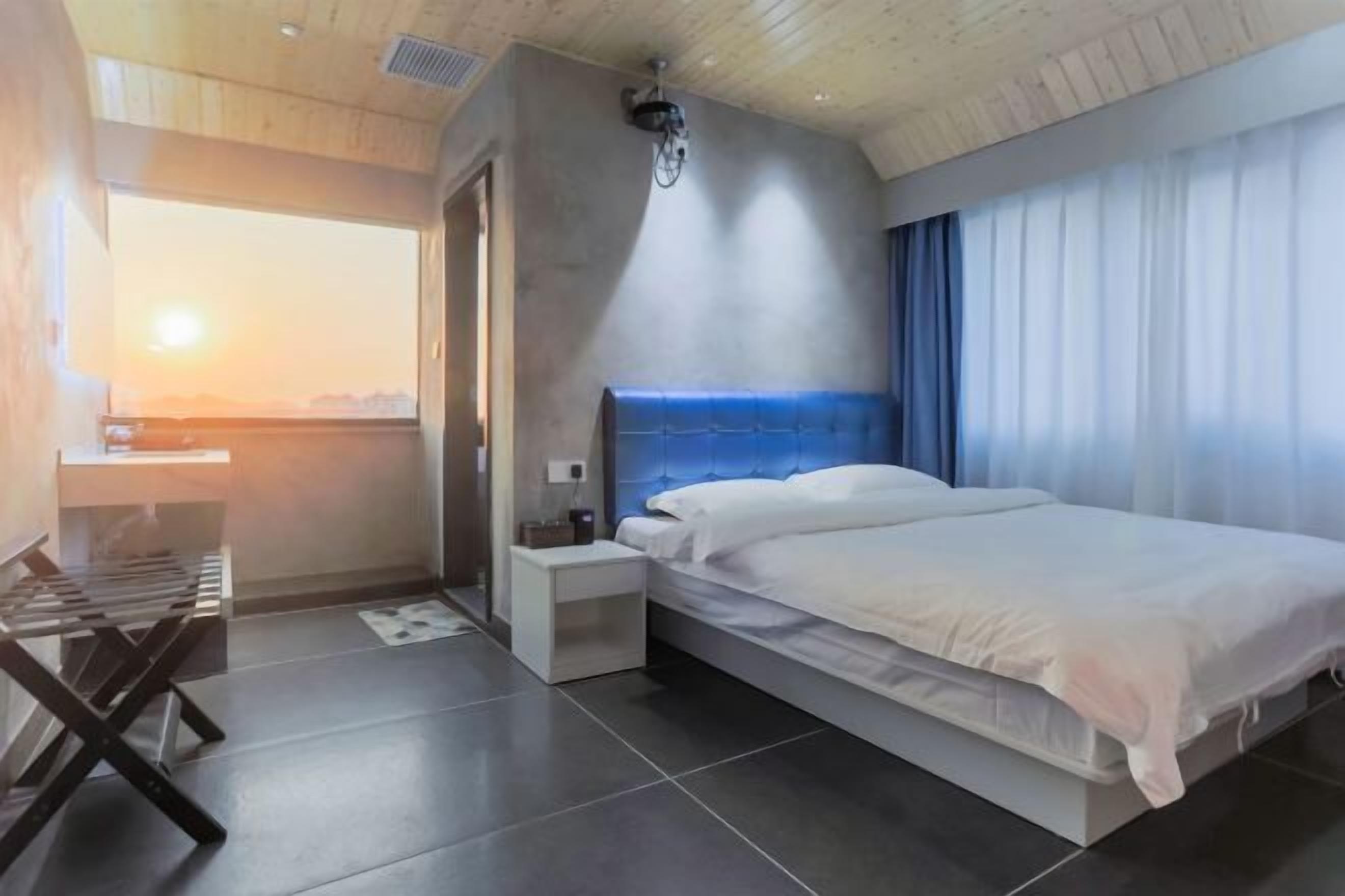 A modern bedroom with a large bed, a nightstand, a bedside table, and a view of the outdoors.