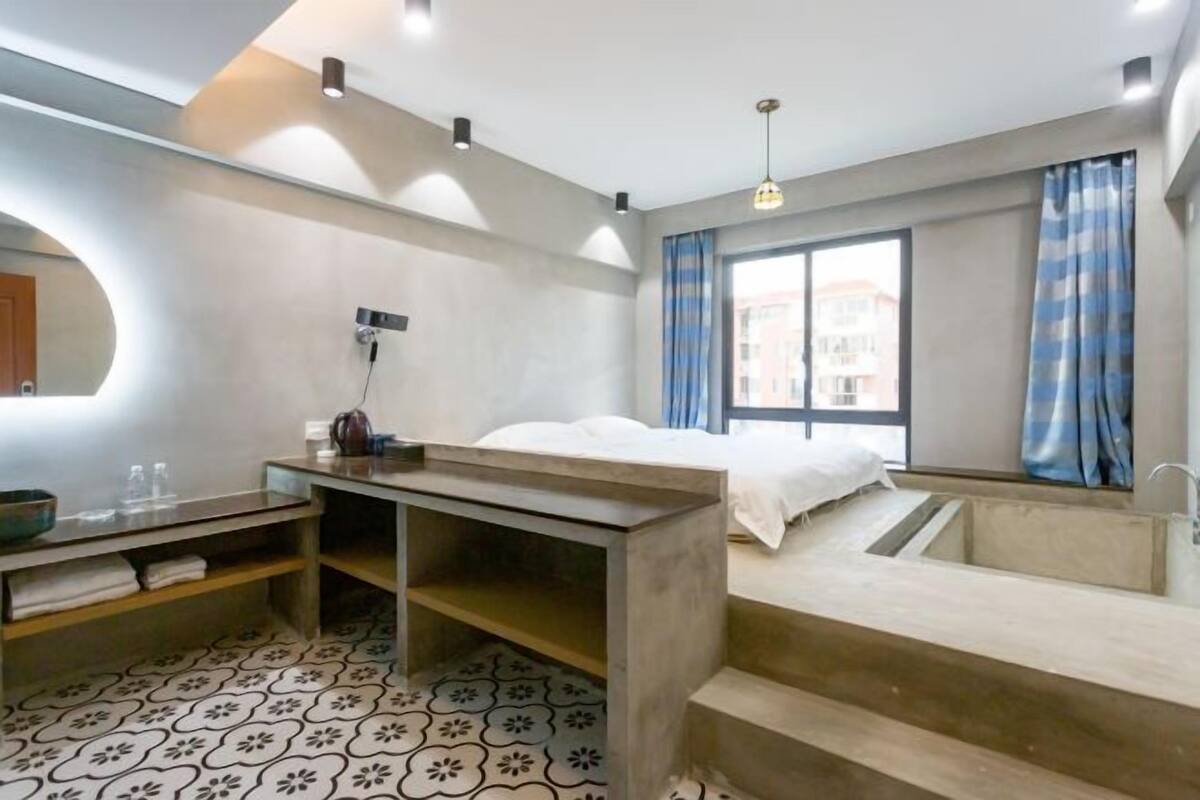 A modern hotel room with a bed, a desk, a sink, and a shower area.
