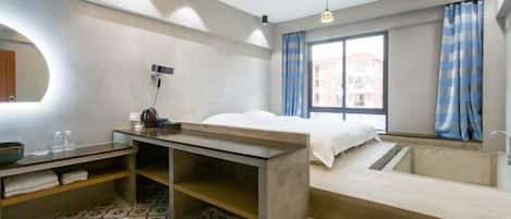 A modern hotel room with a bed, a desk, a sink, and a shower area.