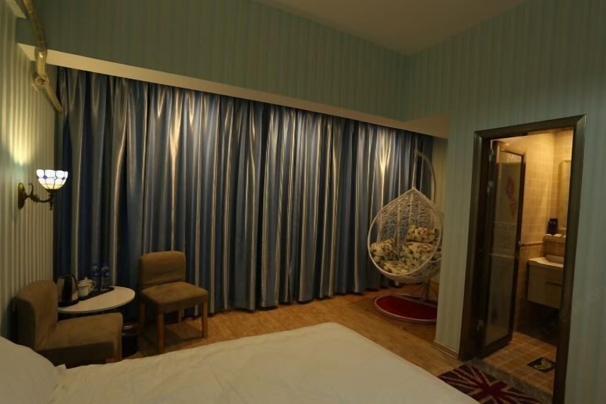 Habitación de hotel con cama, dos sillones, una mesita, un sillón colgante y un baño visible a través de una puerta abierta.