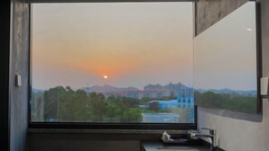 A bathroom with a large window offering a view of a building and trees during sunset. - Dongshan Zhuolan Resort Hotel (Dongshan County)