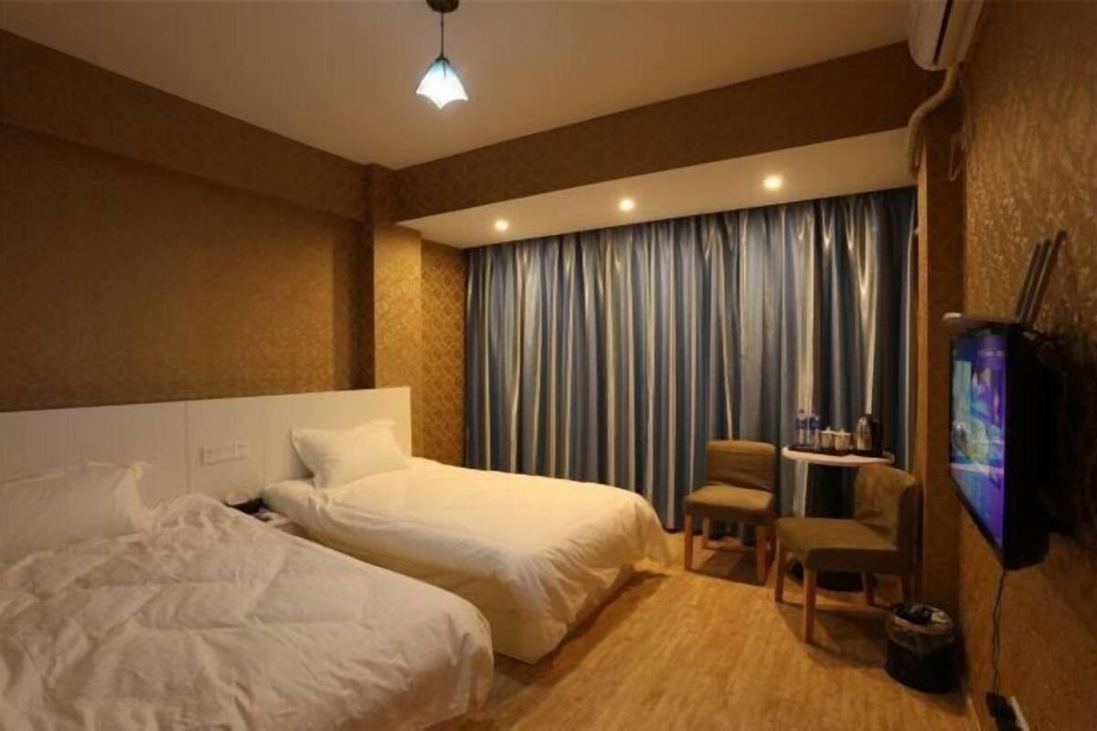 A hotel room with two beds, a desk with a chair, a television, and a curtain.