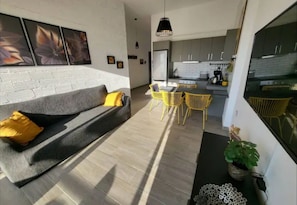 Relax in this inviting space with a sofa, dining area, and kitchen, surrounded by artwork and a potted plant.