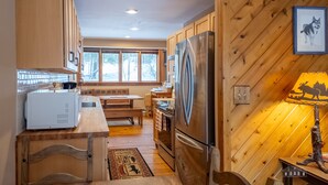 Una cocina con armarios de madera, un refrigerador de acero inoxidable, un microondas blanco y una mesa de comedor de madera.