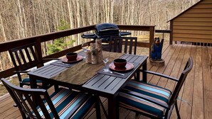 Una terraza de madera con una mesa lista para dos, una parrilla y un letrero de bienvenida.