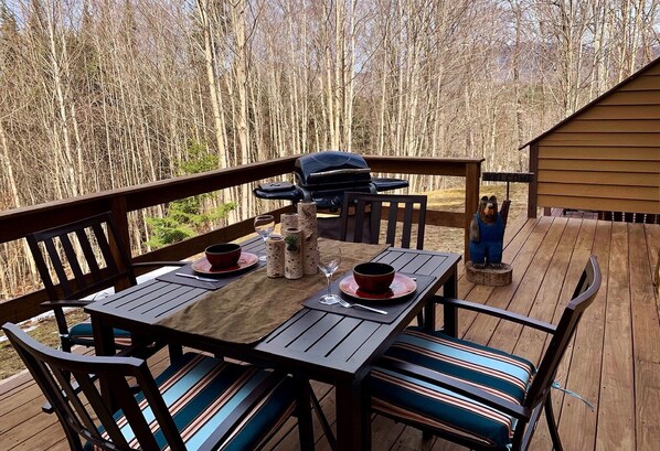A wooden deck with a table set for two, a barbecue grill, and a welcome sign.