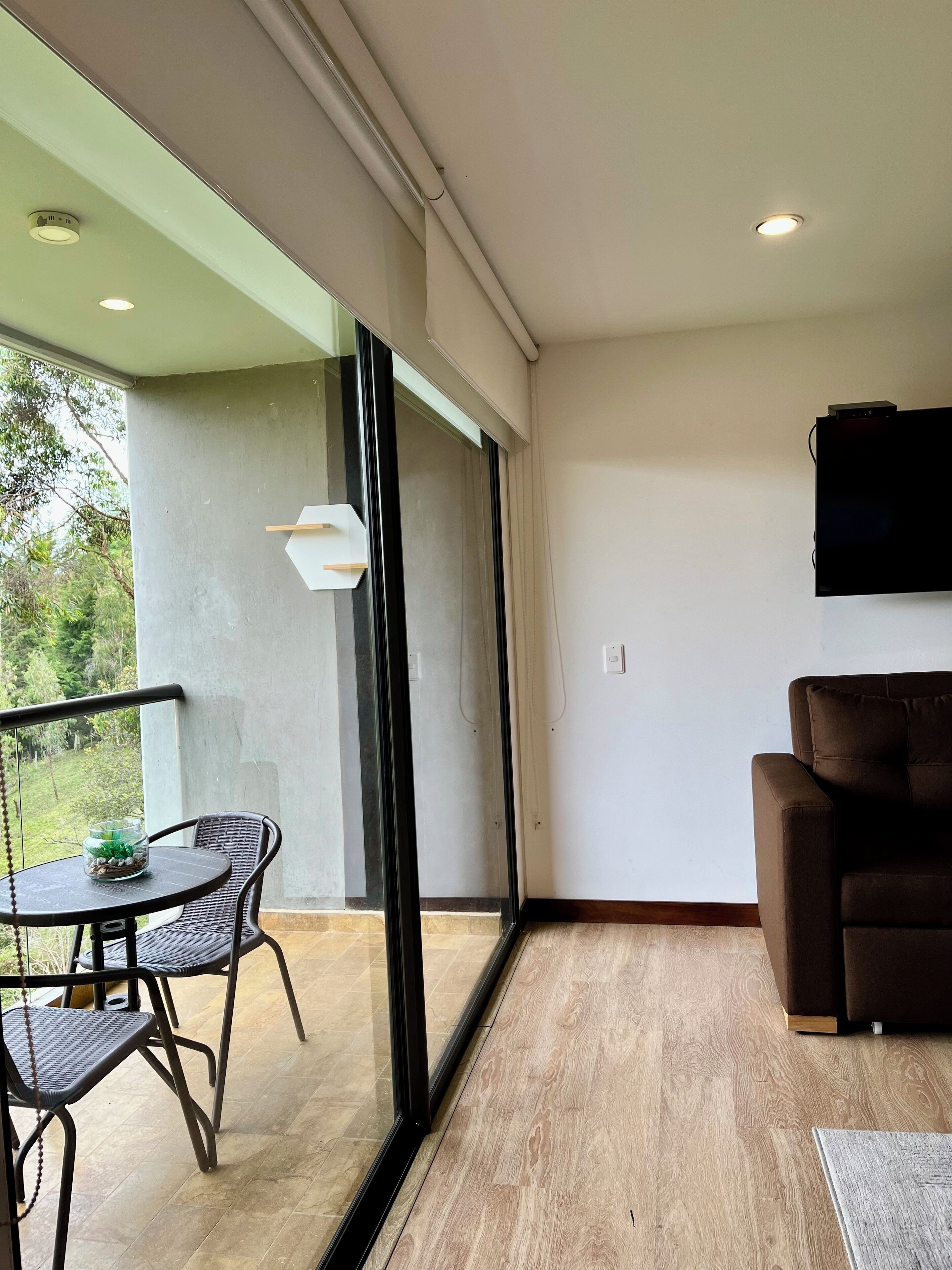 Un salón moderno con un sofá marrón, una mesa de vidrio con sillas y un televisor montado en la pared.