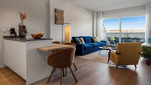 Un salon moderne avec un canapé bleu, un coin repas doté d’une table en bois et une cuisine avec un plan de travail et un vase de fleurs.
