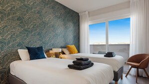 Une chambre d’hôtel avec deux lits, une vue sur la ville et un fauteuil.