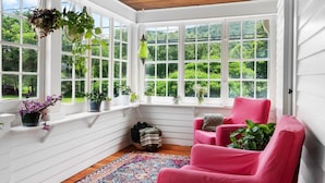 A sunroom with large windows, a wooden ceiling, a pink chair, and various potted plants. - Stylish Historic Home – Timeless Charm with Modern Touches (Bovina Center)