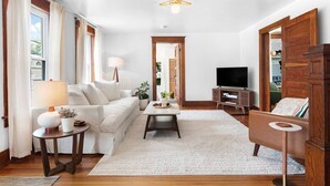 A living room with a sofa, coffee table, TV, and wooden furniture. - Stylish Historic Home – Timeless Charm with Modern Touches (Bovina Center)