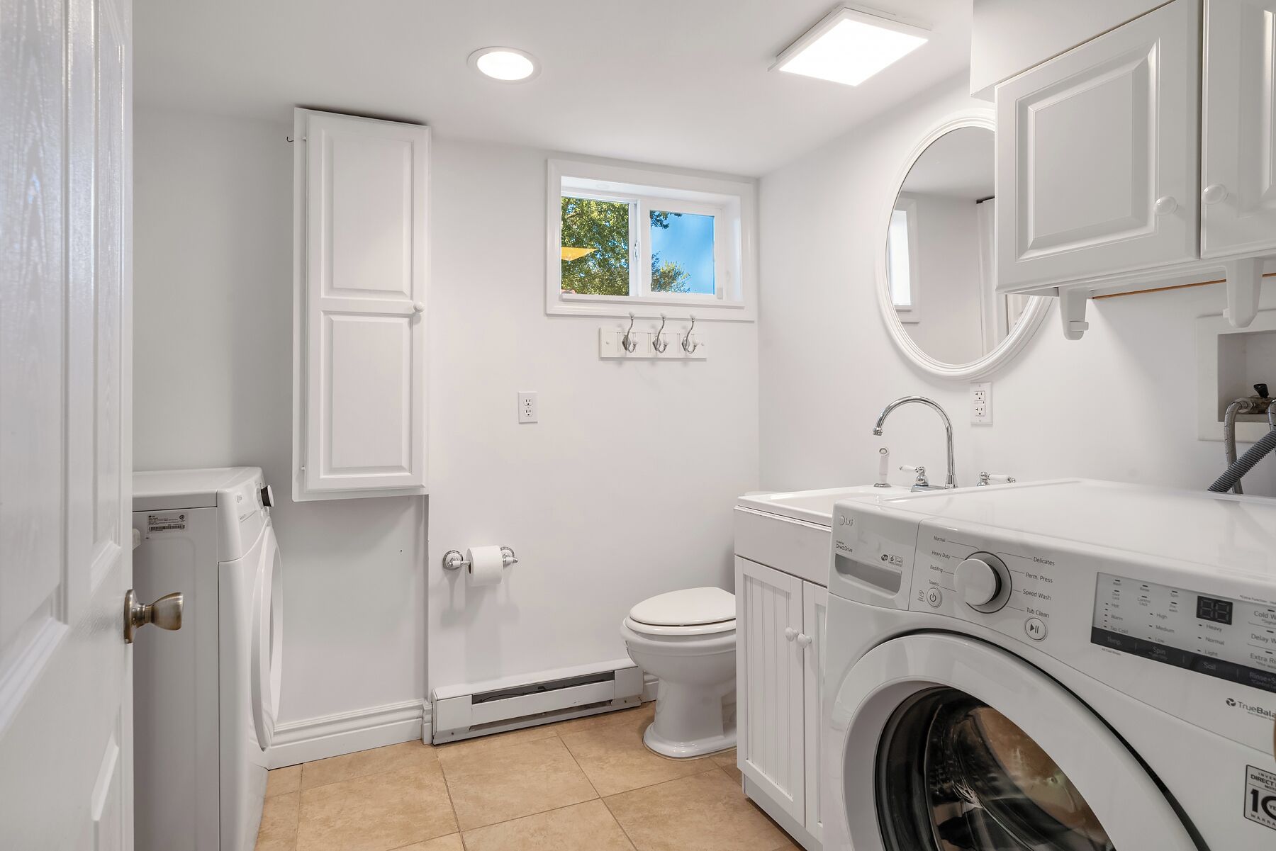 Un baño moderno y funcional con lavadora y secadora integradas, inodoro y ventana con vistas a zonas verdes.