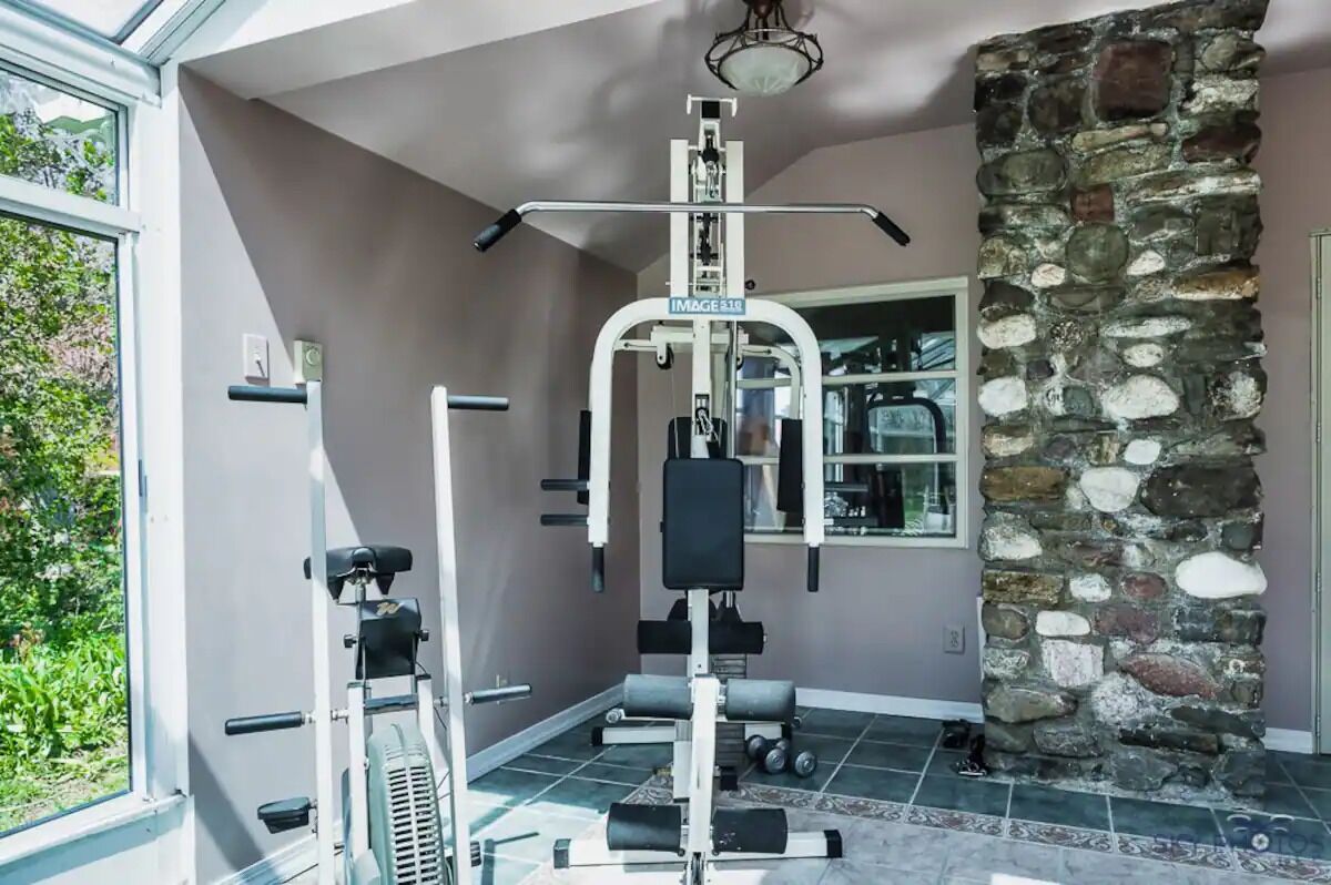 Una palestra in casa con attrezzature per esercizi, un muro in pietra e un'ampia finestra.