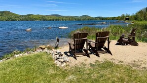 Vista de un lago con sillas y una mesa, rodeado de follaje y colinas.