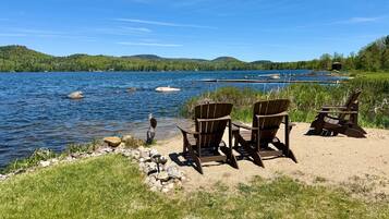 A lakeside view with chairs and a table, surrounded by greenery and hills.