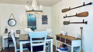 Un espace repas agrémenté d’un lustre, de chaises blanches, d’une table en bois et de pagaies fixées au mur.