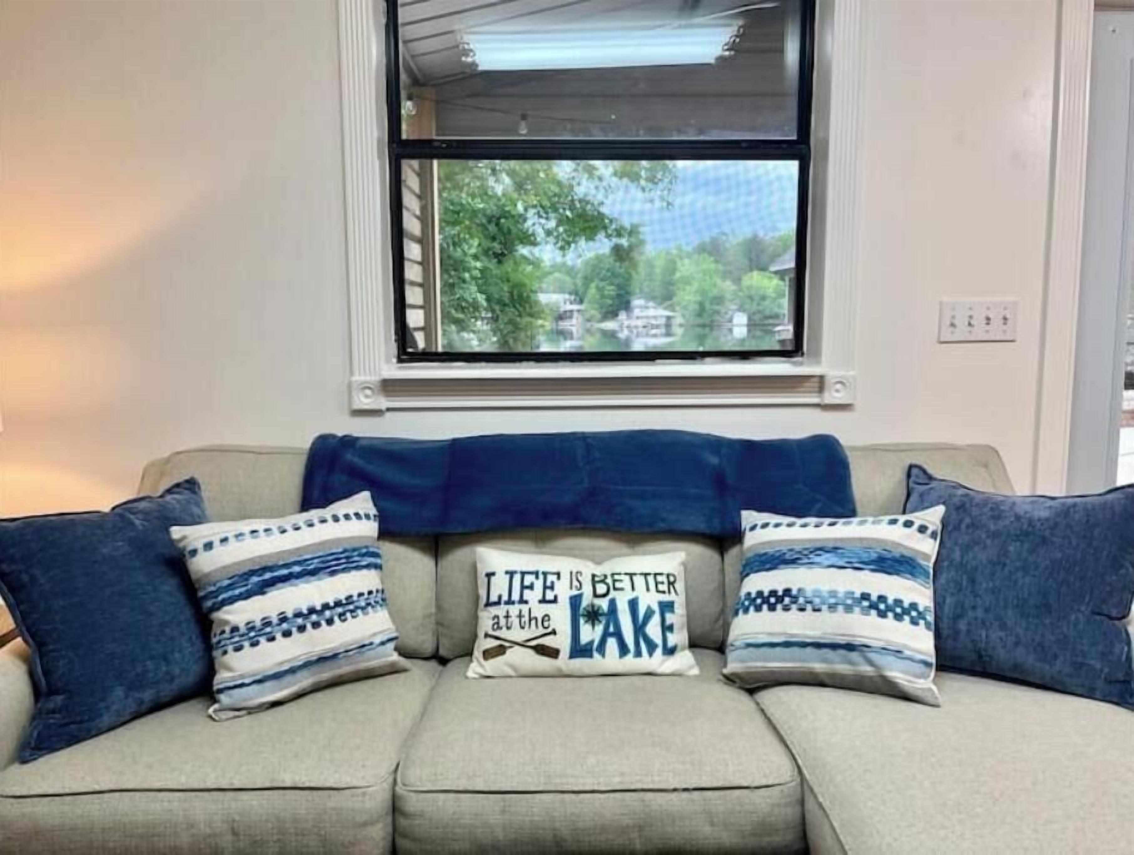 A beige sofa with blue and white patterned pillows, a blue throw blanket, and a window with a view of trees and houses.