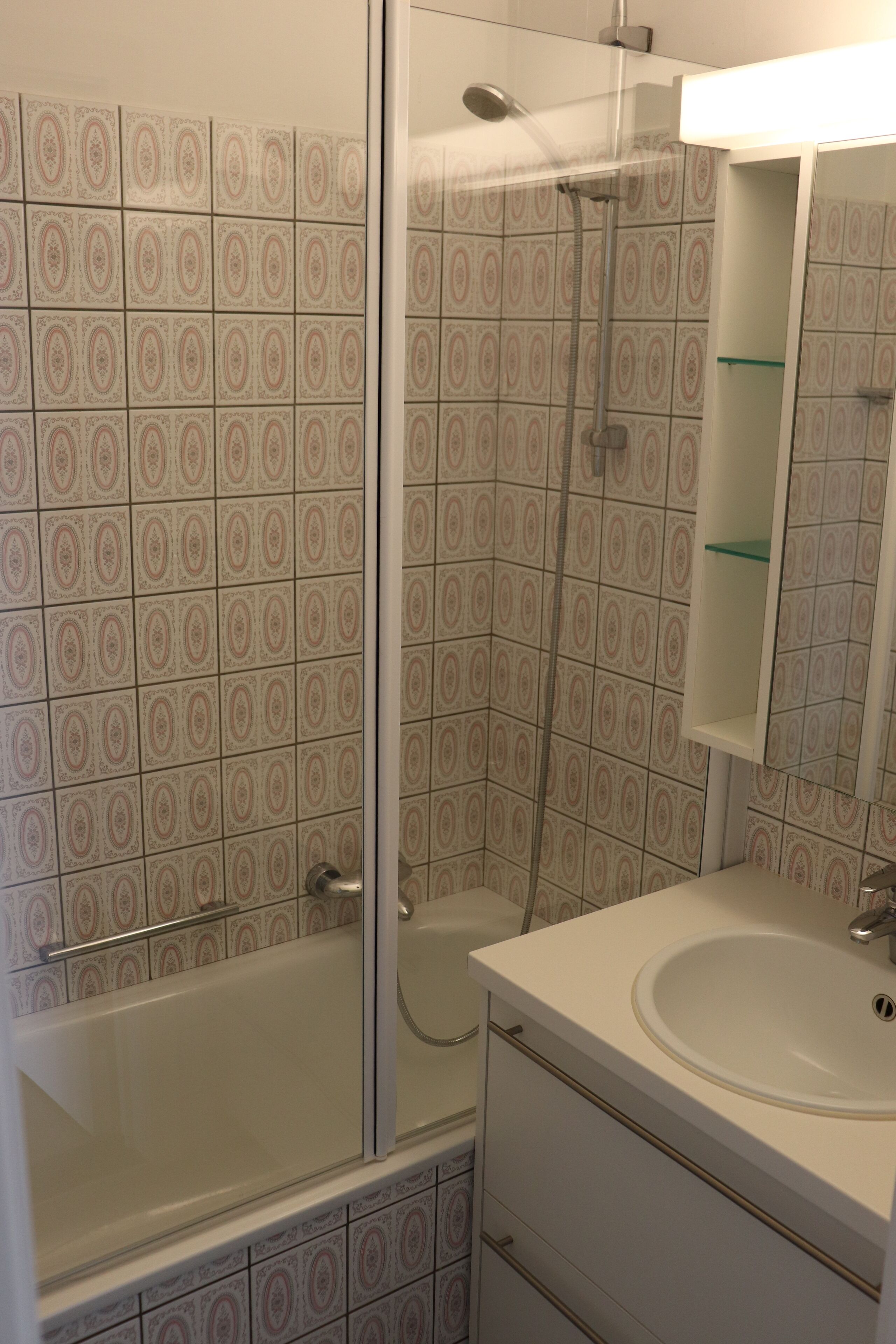 Un bagno con piastrelle decorate, una cabina doccia in vetro, un lavandino bianco e un pensile a specchio.