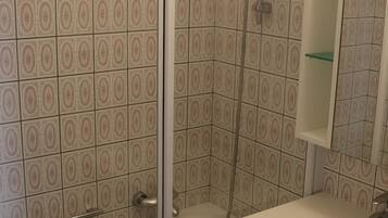 Un bagno con piastrelle decorate, una cabina doccia in vetro, un lavandino bianco e un pensile a specchio.
