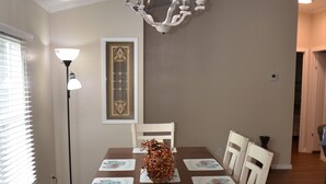 Ein Esszimmer mit Holztisch, weißen Stühlen, einer Chandelüster und einer Stehlampe.