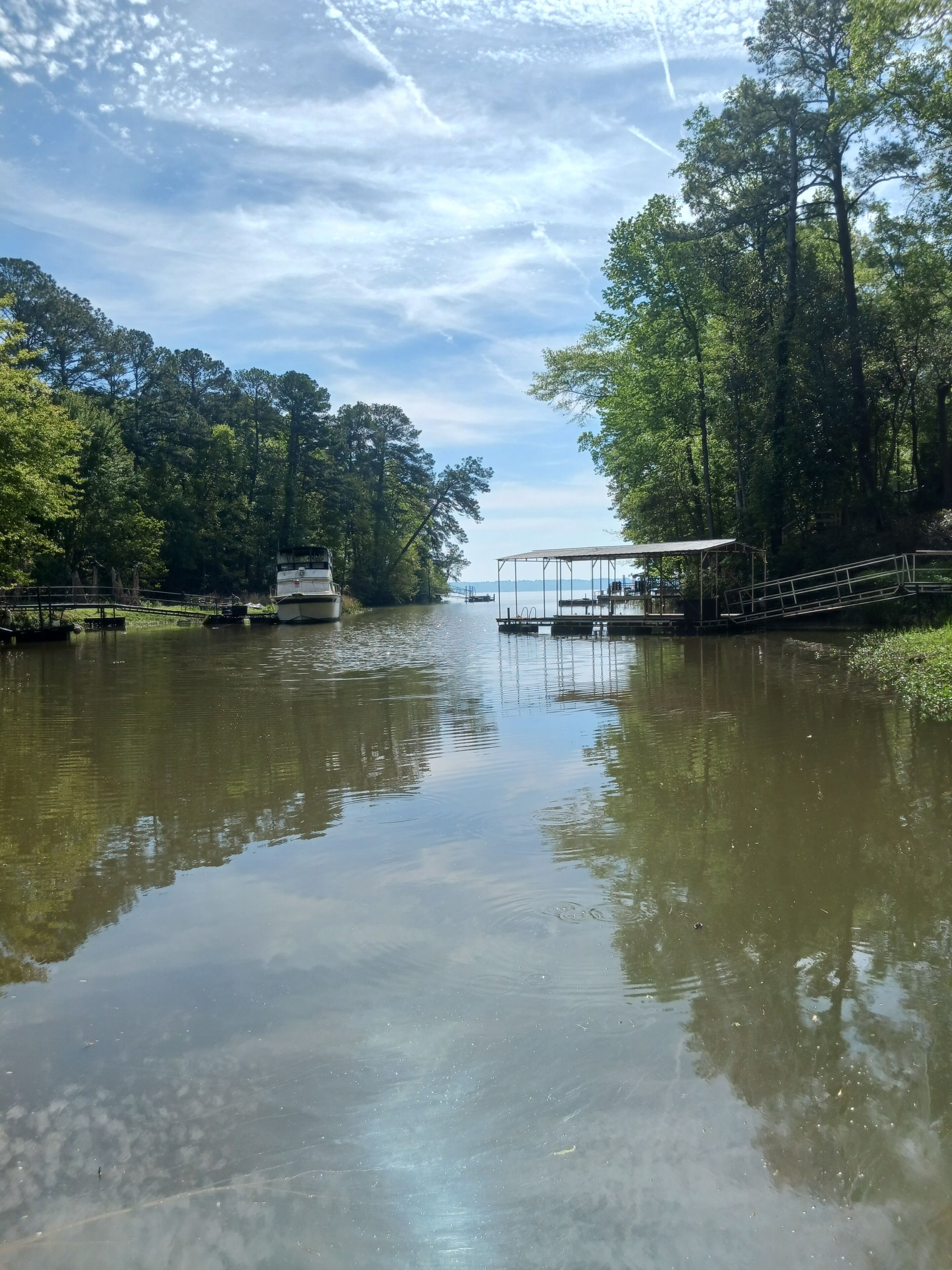 Un río tranquilo con barcos, un muelle techado y árboles densos a ambos lados.